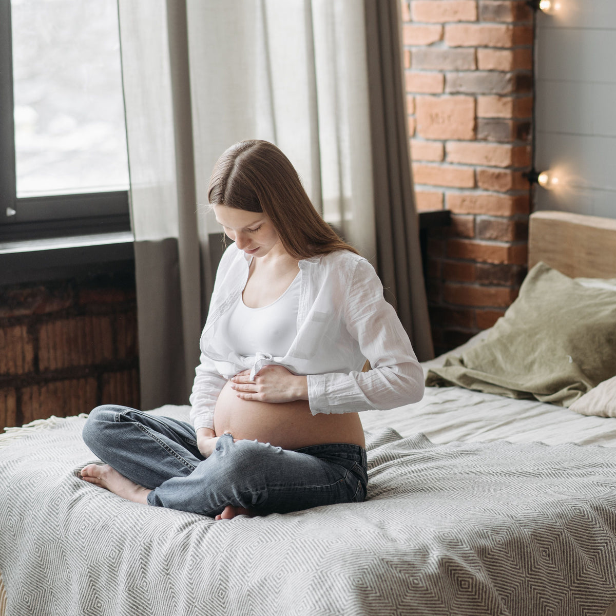 Pregnant woman sitting on a bed in a cozy bedroom.